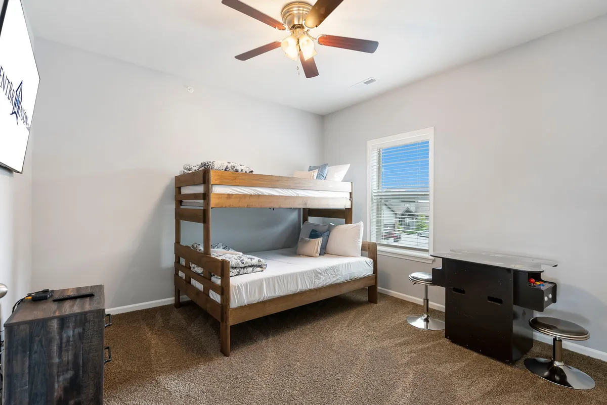 A fun and functional bunk bedroom with a twin-over-full bunk bed, a desk area for study or play, and a window letting in sunlight. The space is designed for kids or groups, combining coziness with playful practicality.