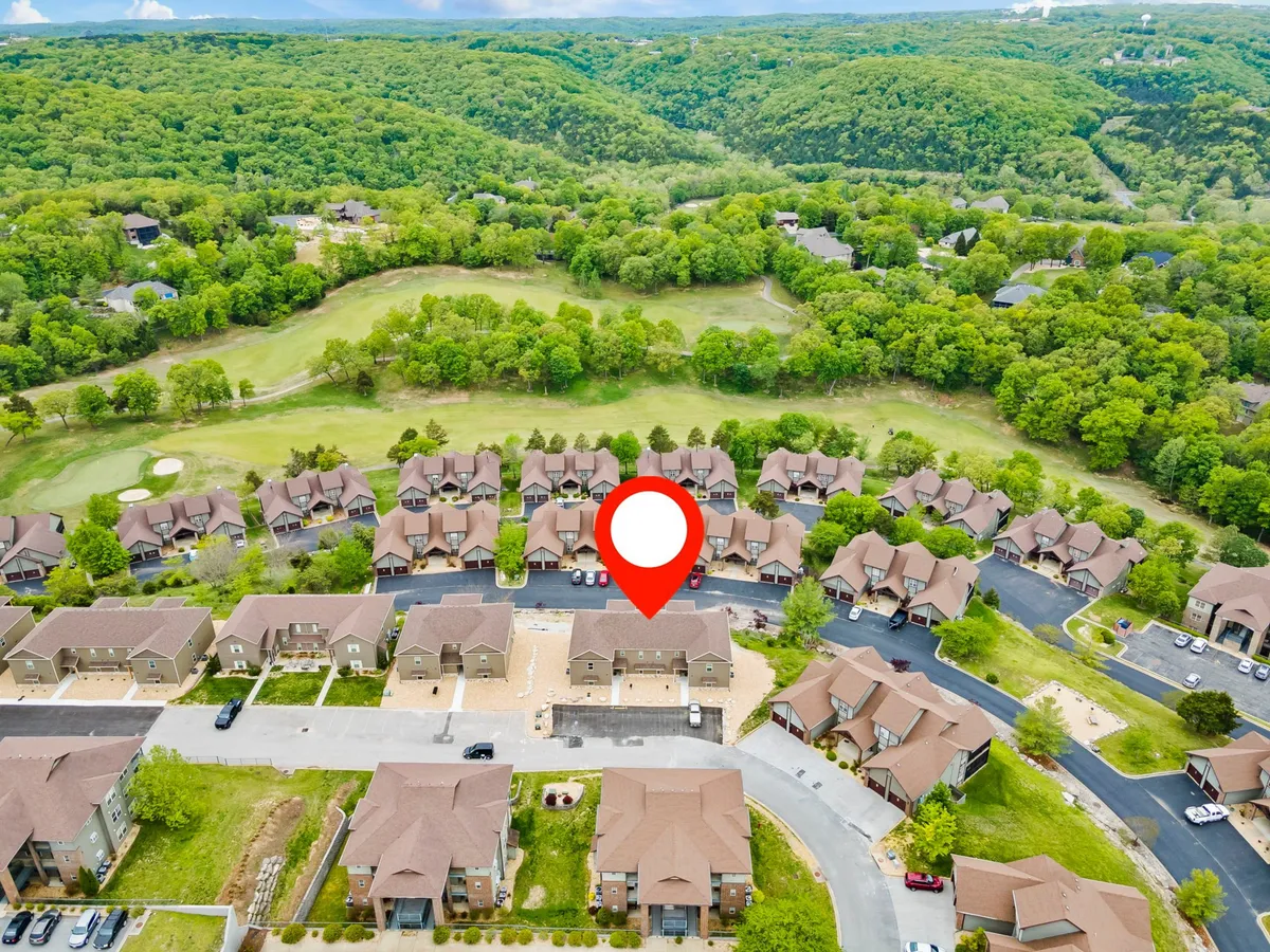 This image provides a distant, inviting view of the golf course set against lush greenery and a sunny sky, with the surrounding neighborhood in the foreground. It evokes a relaxed, community-oriented atmosphere and a sense of place.