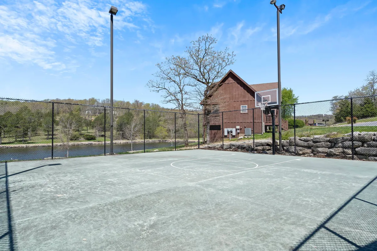 This image features a basketball court surrounded by lush greenery, with a distant view of a water body and a house in the background. The court is well-maintained, inviting for group sports, and the setting captures the active, outdoor lifestyle available to guests.