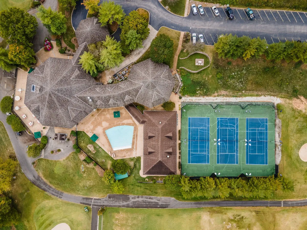 This exterior image captures a vibrant resort scene featuring a swimming pool, tennis courts, the main building, and lush surrounding greenery. The pool area is active and inviting, perfect for families enjoying summer days, while the tennis courts suggest opportunities for friendly matches and group activities.