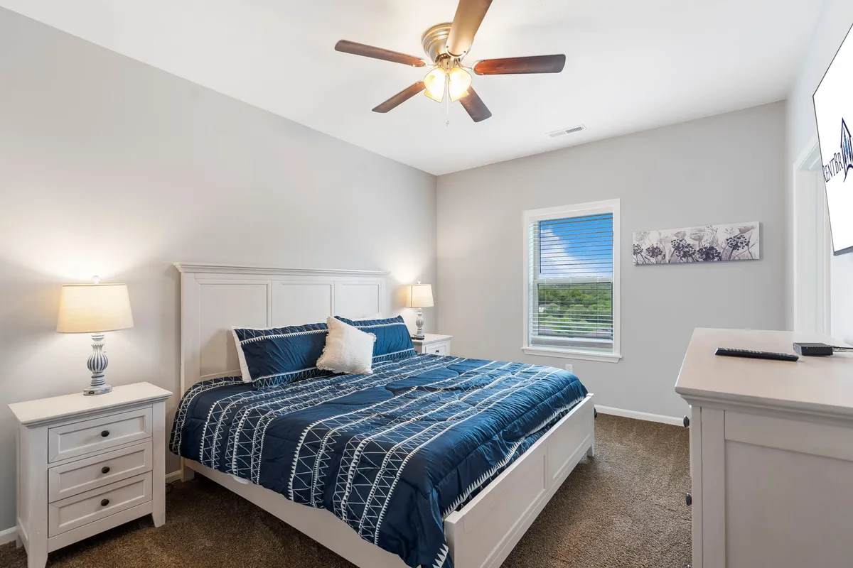 A bedroom featuring a bed with blue bedding, a nightstand with a lamp, and a window offering views and natural light. The atmosphere is peaceful and uncluttered, creating an inviting place to relax and recharge.