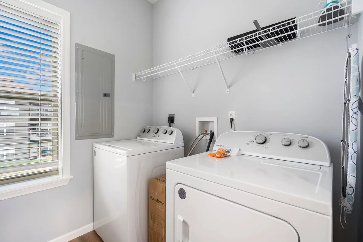 A clean, well-lit laundry area is outfitted with a modern washing machine, drying machine, and an organized storage shelf filled with essentials. The space exudes a sense of professionalism and order.