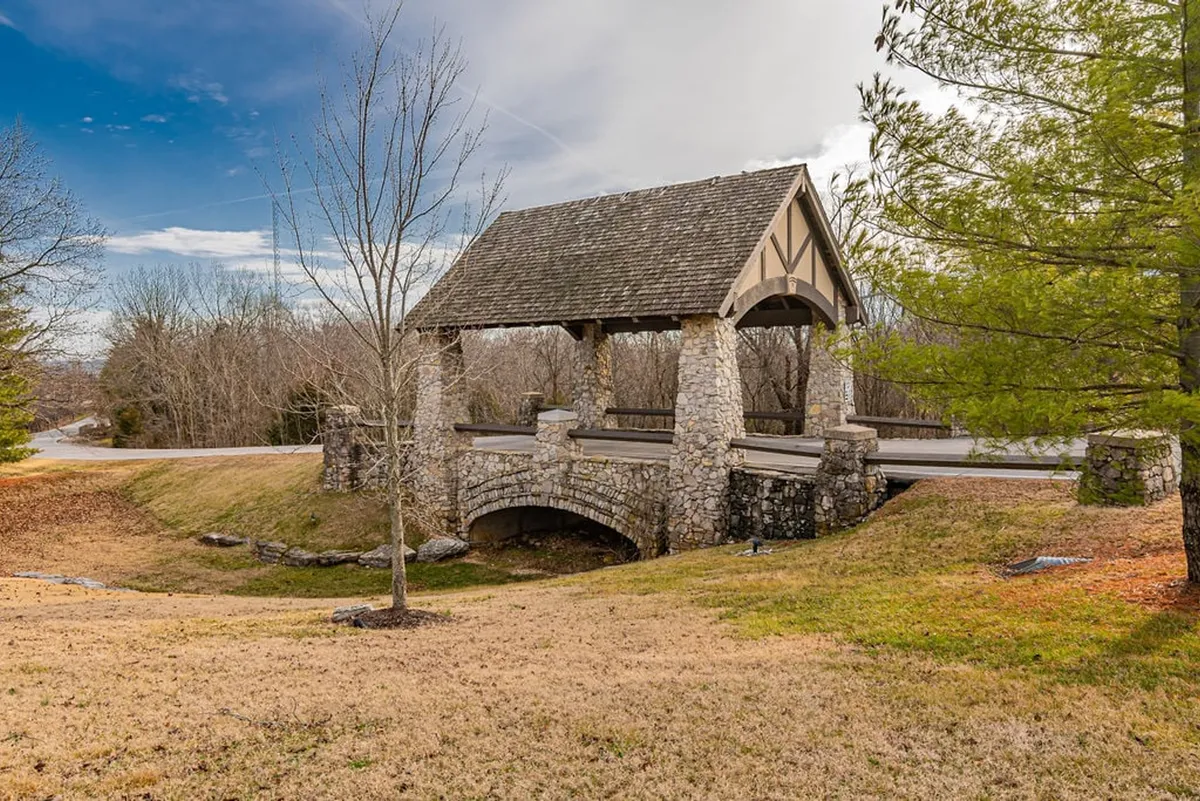 A tranquil exterior landscape featuring a charming stone bridge, surrounded by lush trees and an open grassy area, bathed in the warm glow of sunset. The serene mood and expansive setting invite peaceful walks and moments of quiet reflection in nature.