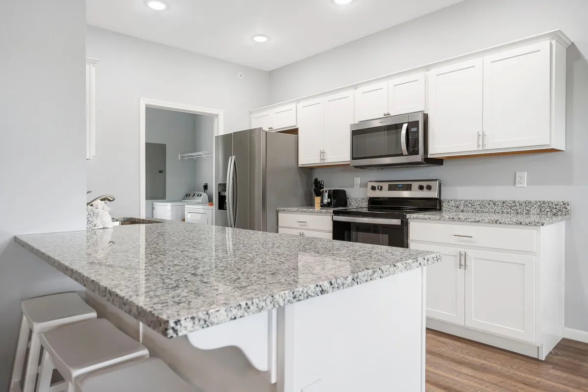 A modern kitchen shines with granite countertops, stainless steel appliances, and crisp white cabinetry. The layout is open and functional, ideal for preparing meals and socializing. The overall mood is clean, bright, and contemporary.