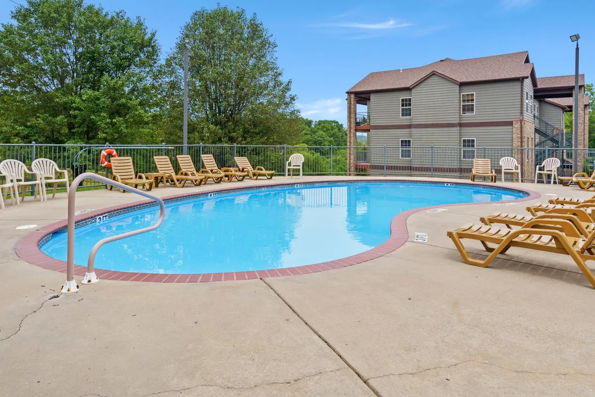 A leisurely pool area surrounded by lounge chairs, mature trees, and a building in the background. The pool is a focal point for relaxation, and the warm, soft light hints at late afternoon or early evening, inviting guests to unwind and connect.