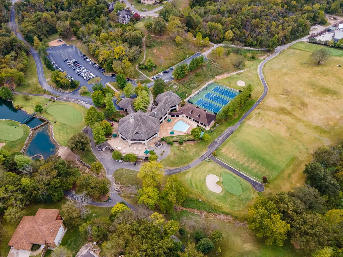 An aerial view capturing the main building, championship golf course, tennis courts, swimming pool, and pond, all surrounded by lush greenery. The scene showcases the scope and quality of the resort’s amenities and recreational spaces.