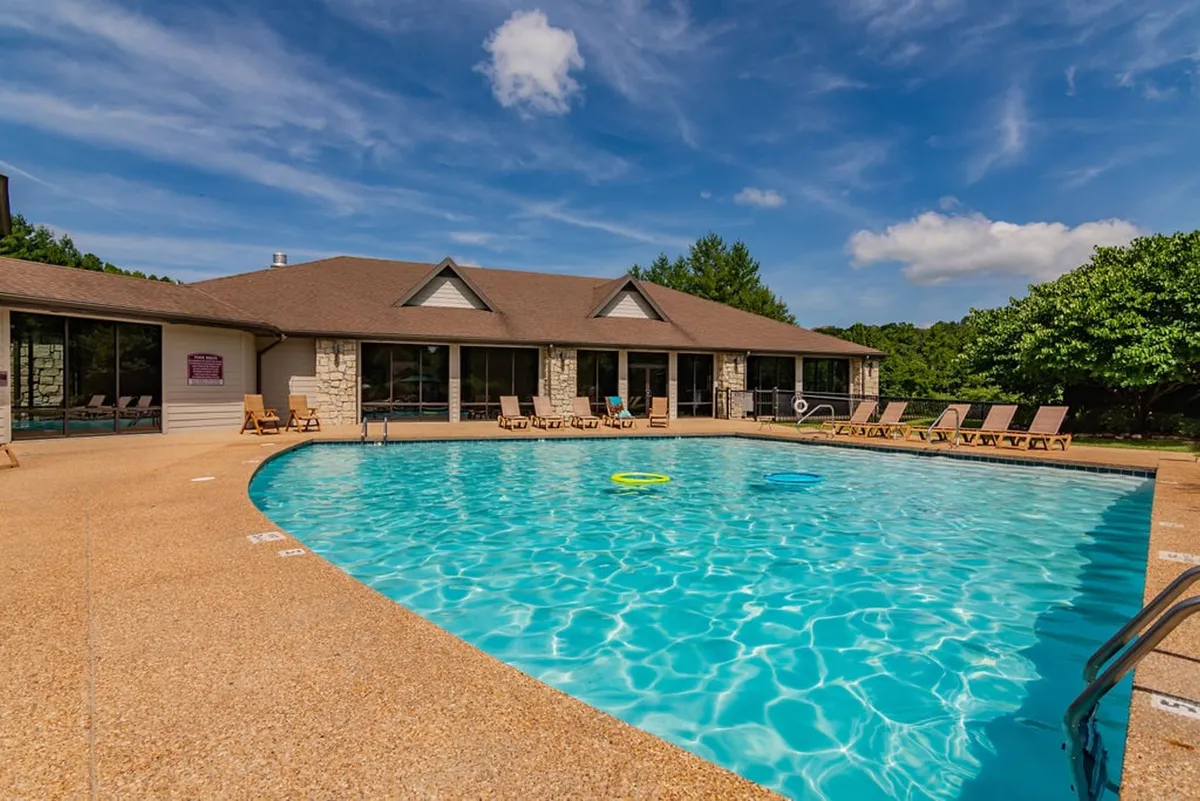 A sunlit resort pool area framed by lounge chairs and a building with large windows. The setting is vibrant with opportunities for swimming, sunbathing, and socializing, evoking the atmosphere of a luxury vacation escape.