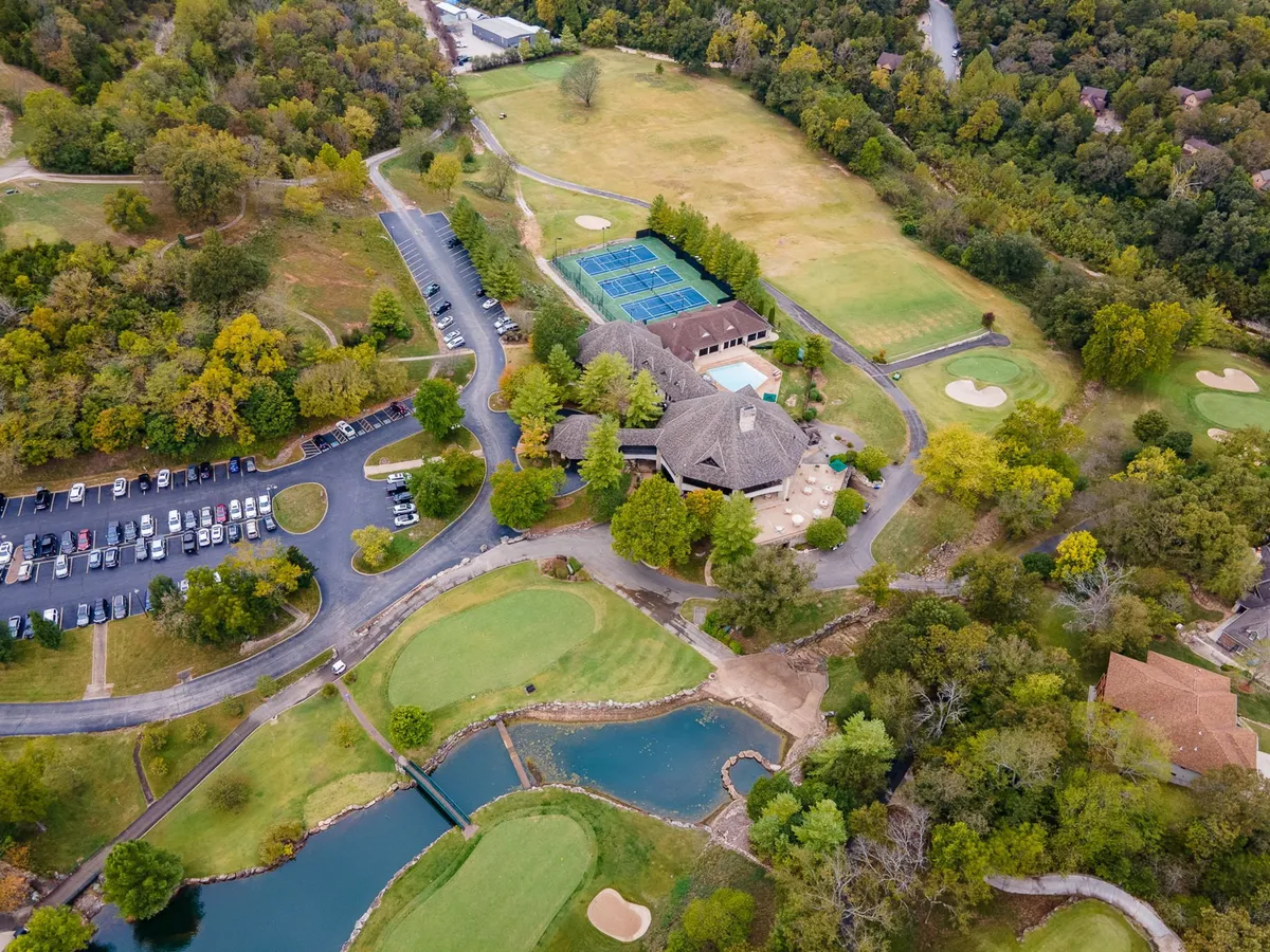 A sweeping exterior shot showcasing the golf course alongside tennis courts, the main resort building, parking areas, and tranquil ponds. The environment is active, social, and well-integrated with resort amenities.